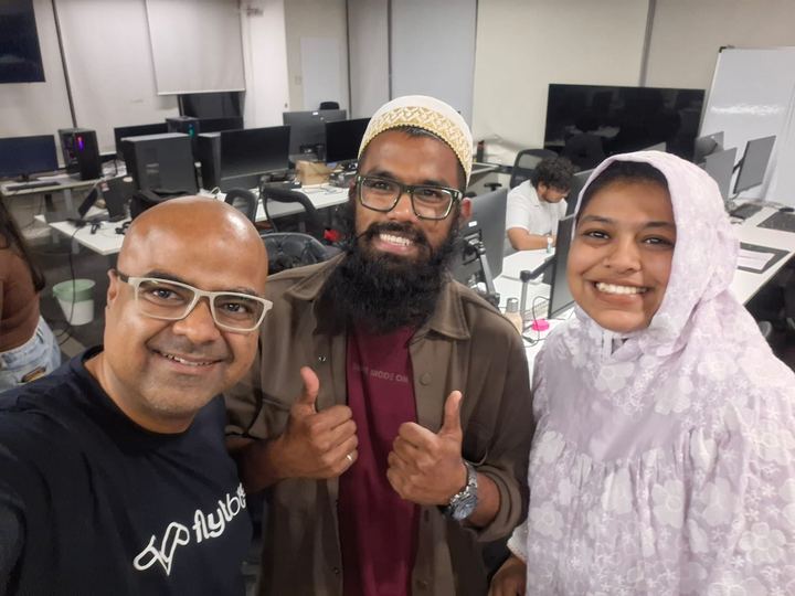 Two colleagues taking a selfie with a guest in a busy tech office