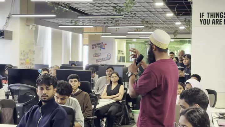 A speaker addressing a seated room of attendees inside an office